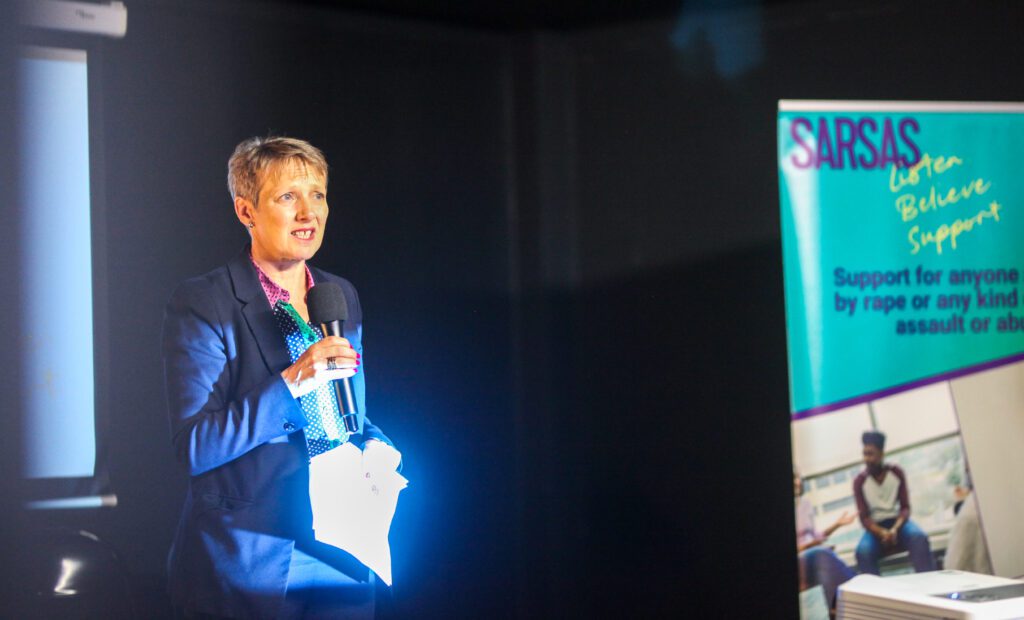 Claire Moody Police Crime Commissioner standing on a stage next to a SARSAS banner speaking into a microphone.
