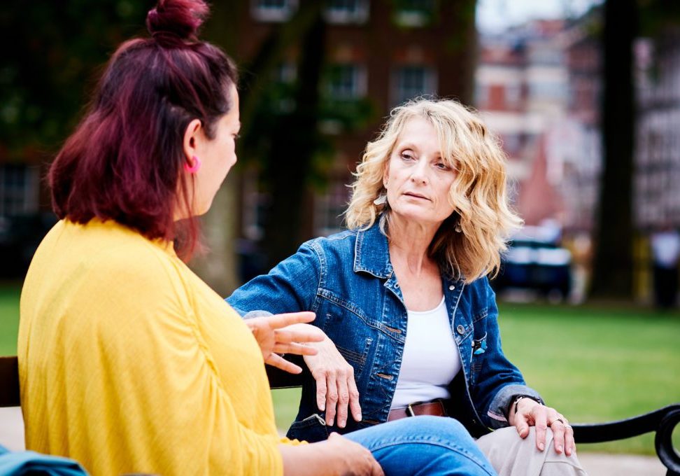 Two women talking on a bench in a park