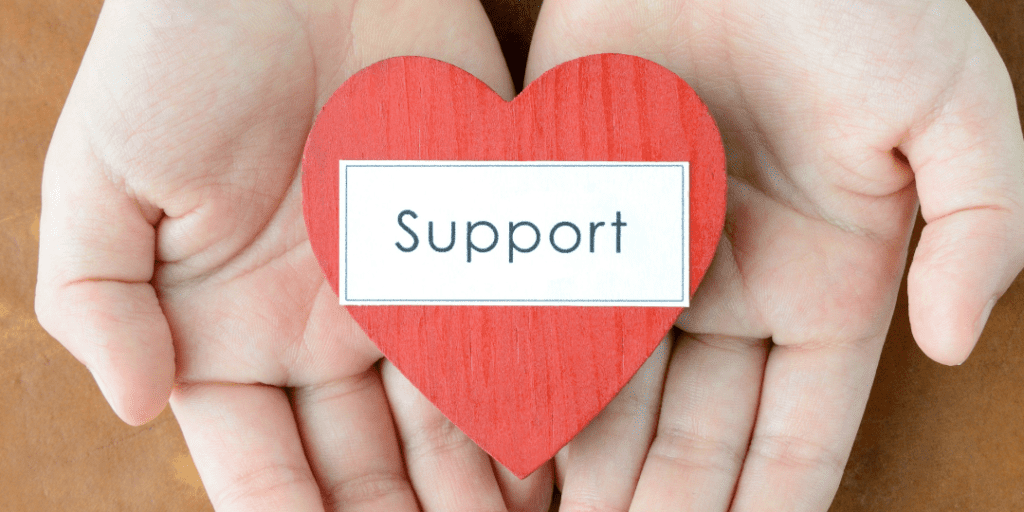 Hands holding the word support written down on a piece of paper shaped as a heart
