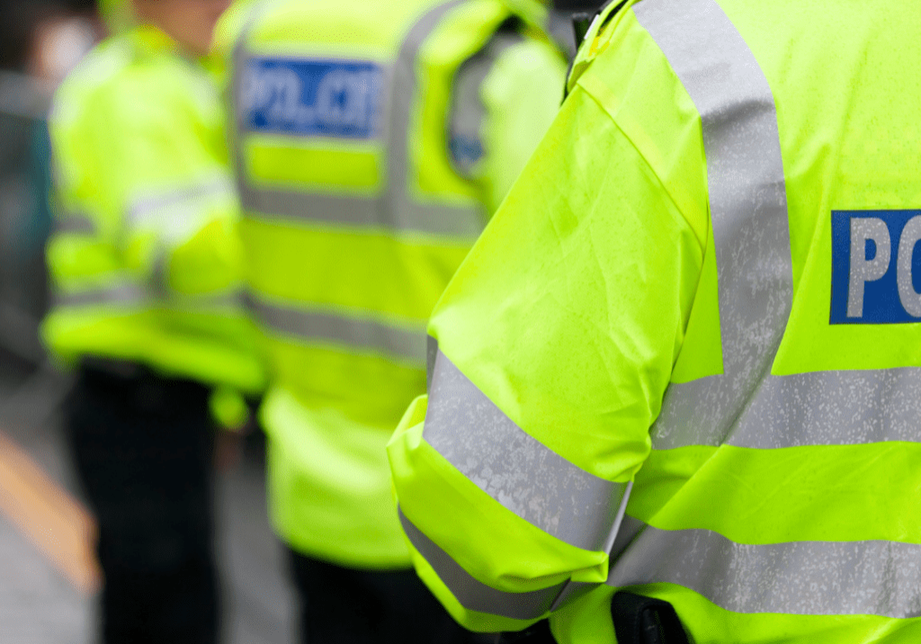 A photo of three police officers. You can only see their backs. They are wearing yellow high visibility jackets with the word 'Police' on them.