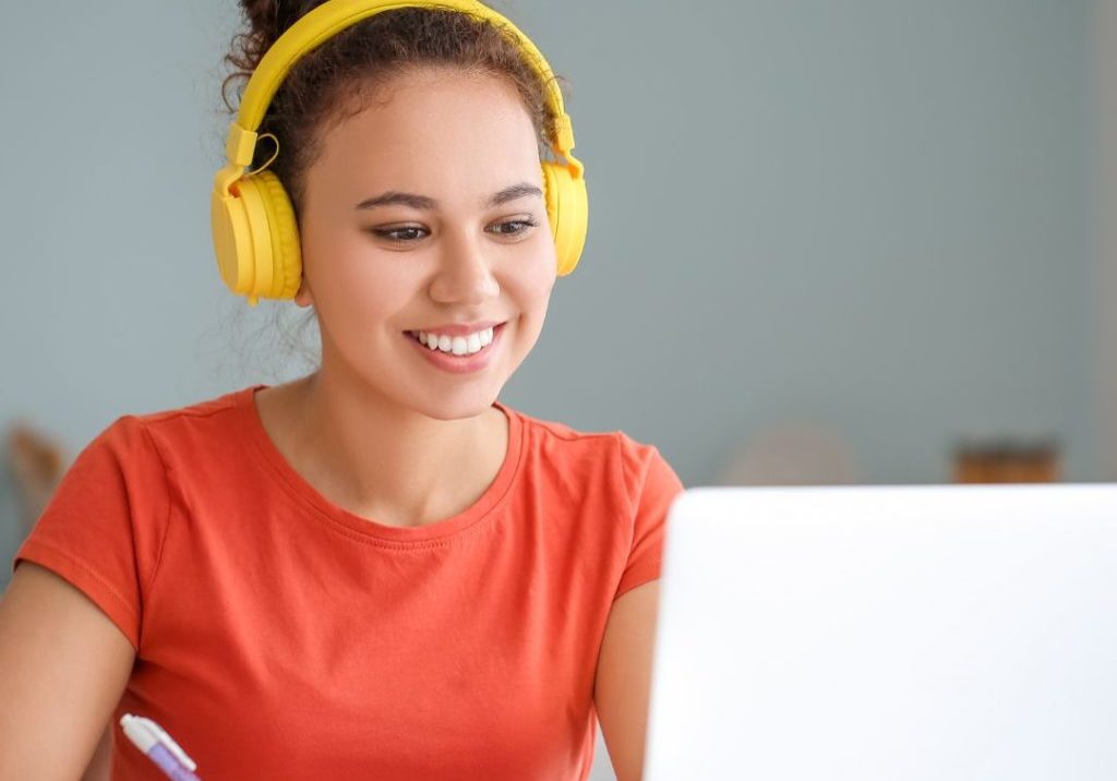 Untitled design (1) women with headphones on taking notes from her laptop