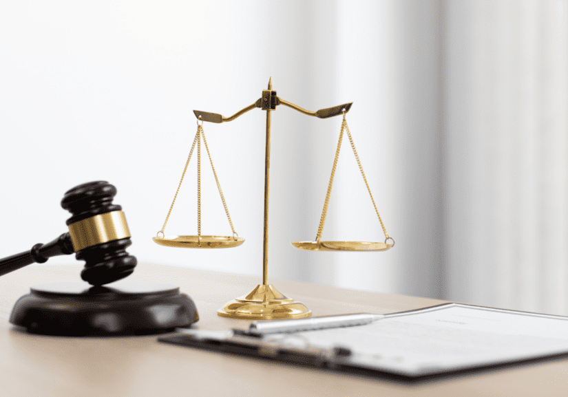 Bronze scales on a desk next to open notebook and judges hammer.