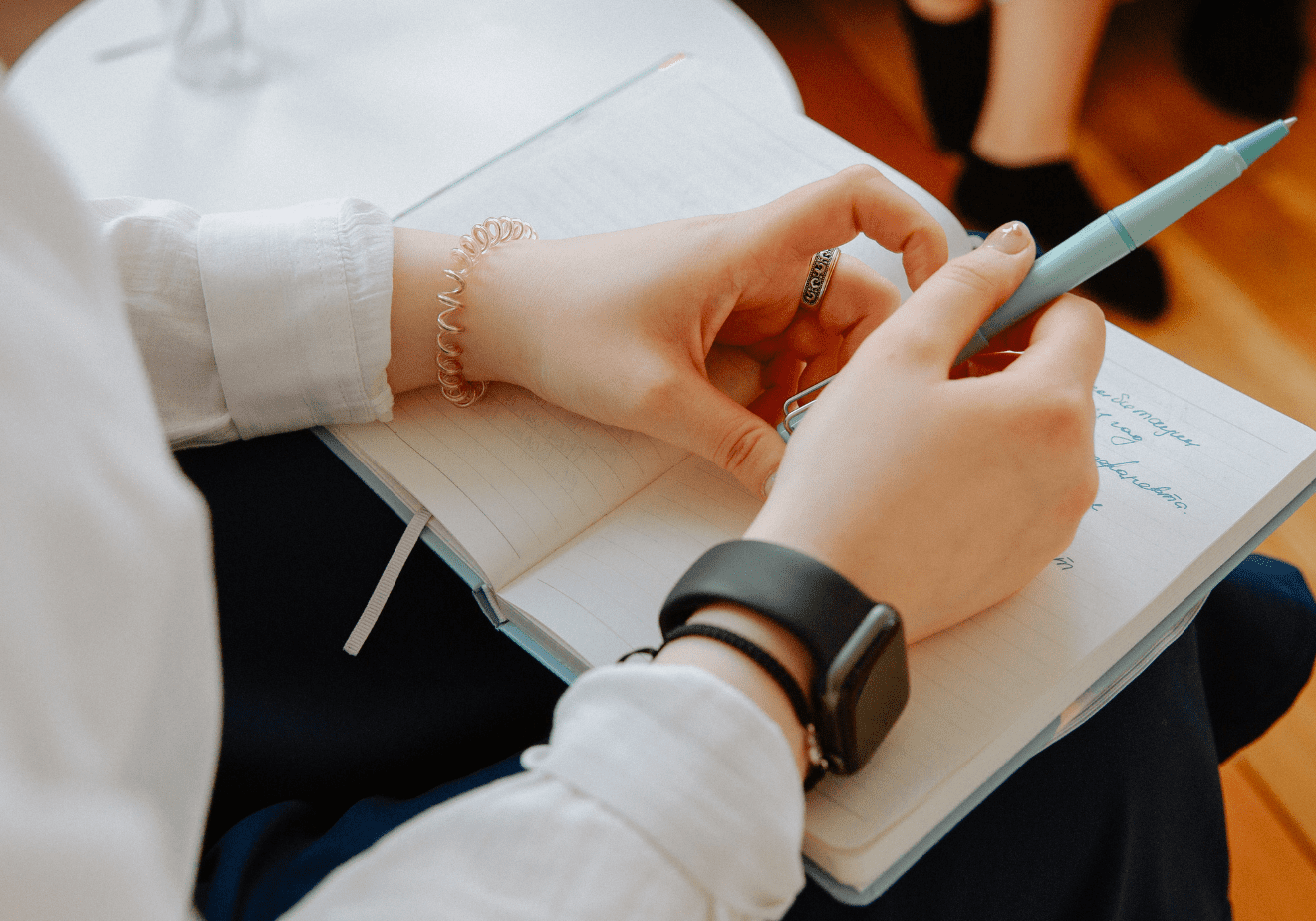 A woman is looking at a notepad in her lap. She has a pen in her hands.