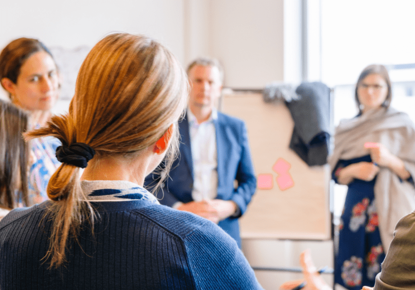 A workshop standing in a circle around a flip chart