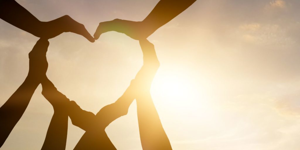 A photo of peoples hands forming a love heart with sky in background