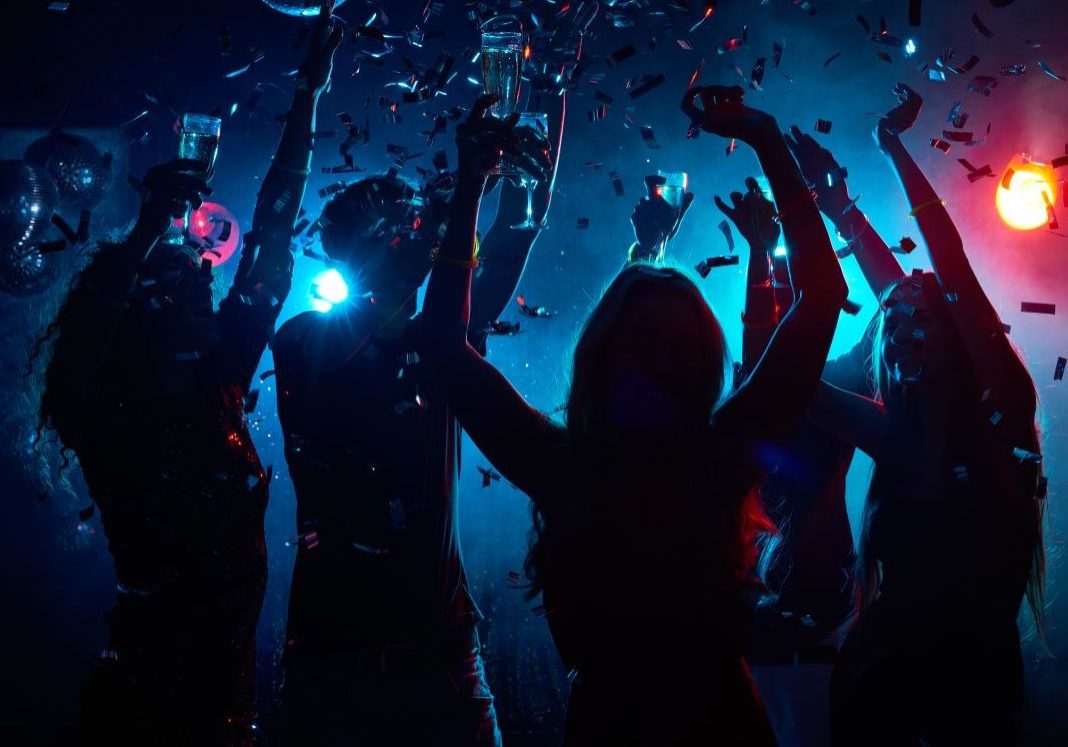 Untitled design - 1 silhouettes of people with arms up in a blue room with red lights dancing