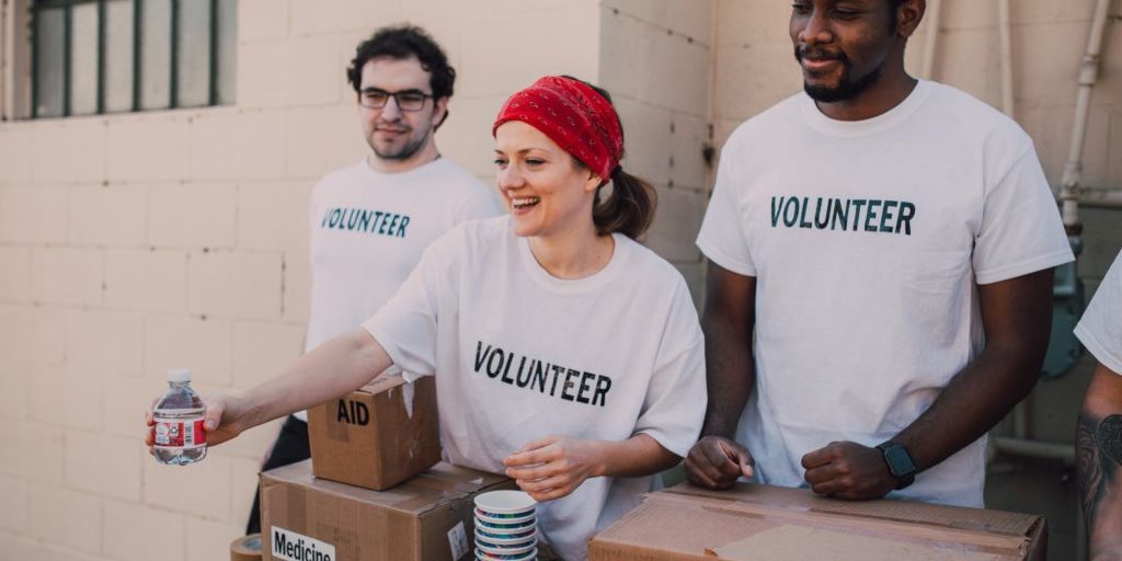 pexels-rodnae-productions-6646918 Three volunteers are handing out supplies. There is a white man with glasses, a white woman with a re headband, and a black mand with a goatee beard.