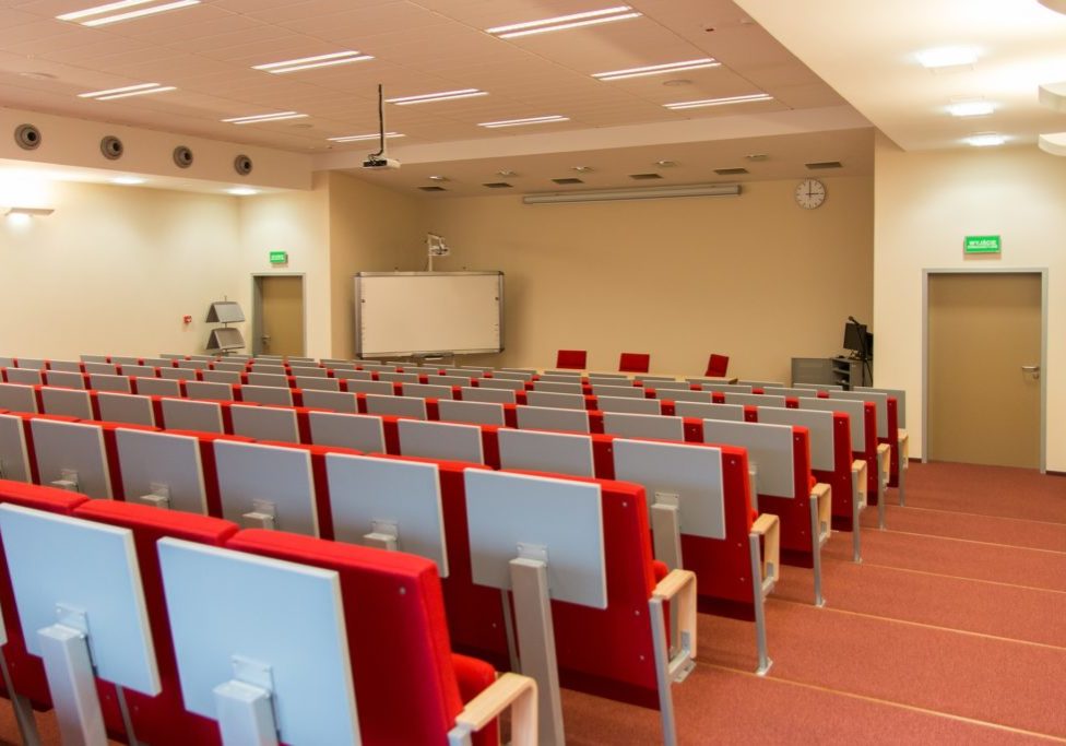 An empty lecture room with red chairs.