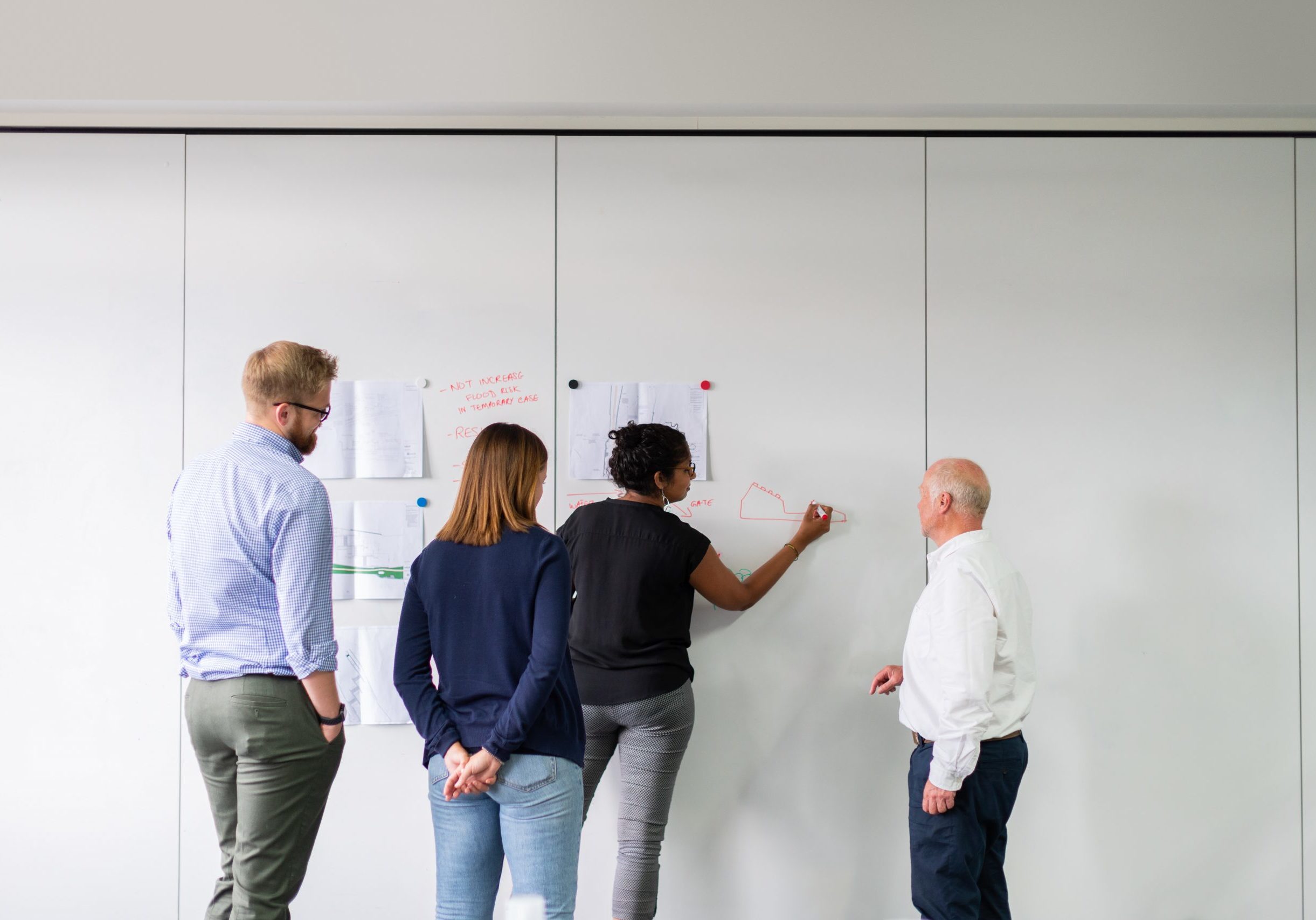 A group of people in office clothes are writen nots on paper stuck to a wall. They are working something out.