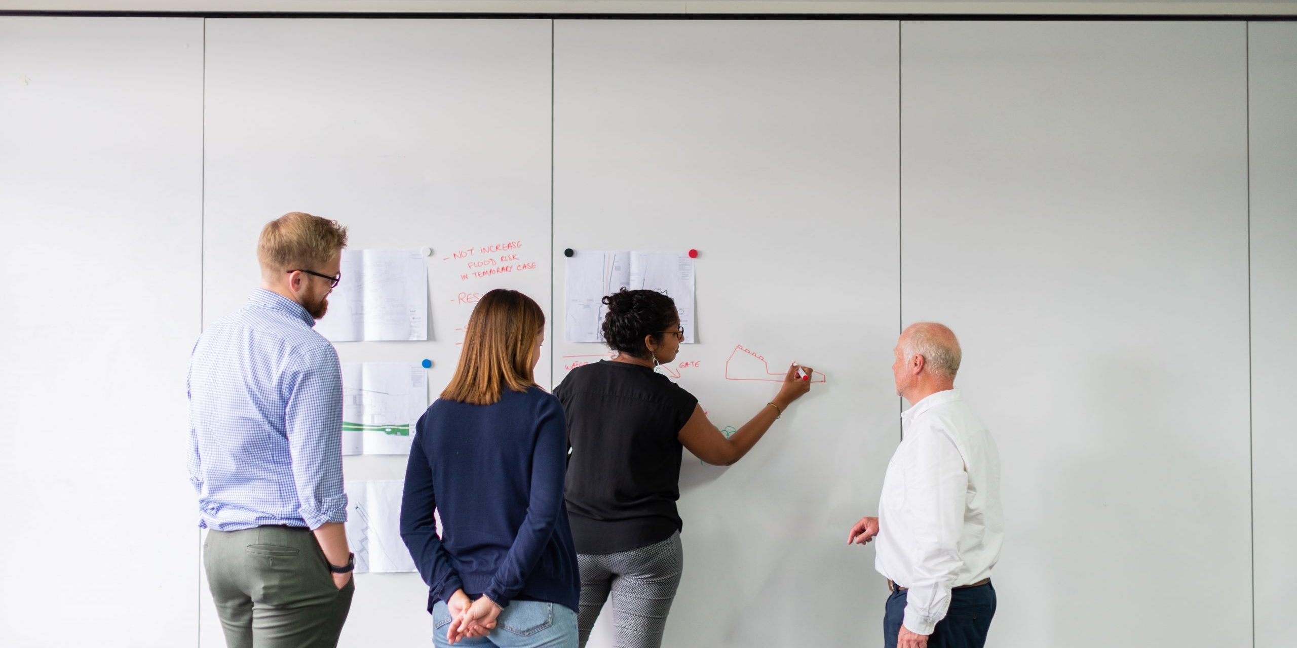 A group of people in office clothes are writen nots on paper stuck to a wall. They are working something out.